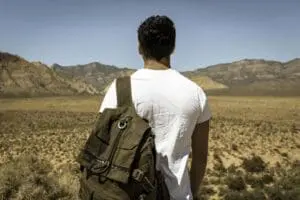 Man with backpack facing desert landscape.