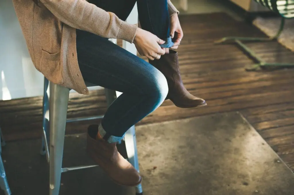 Person sitting, adjusting brown ankle boots.