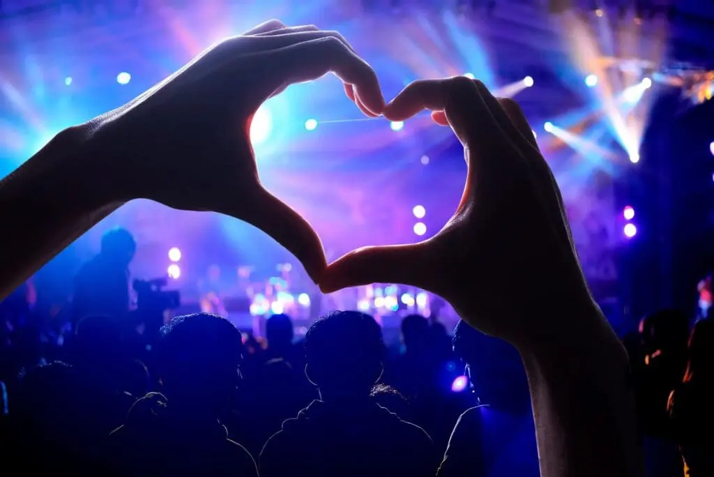 Hands forming heart at concert, colorful lights.