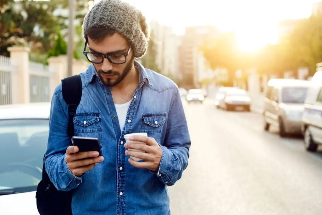 Man with phone and coffee on street.