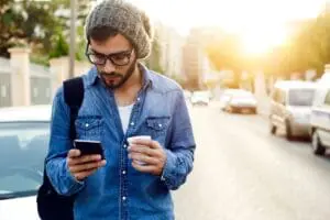 Man with phone and coffee on street.