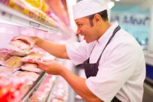 Butcher arranging meat packages in display case.