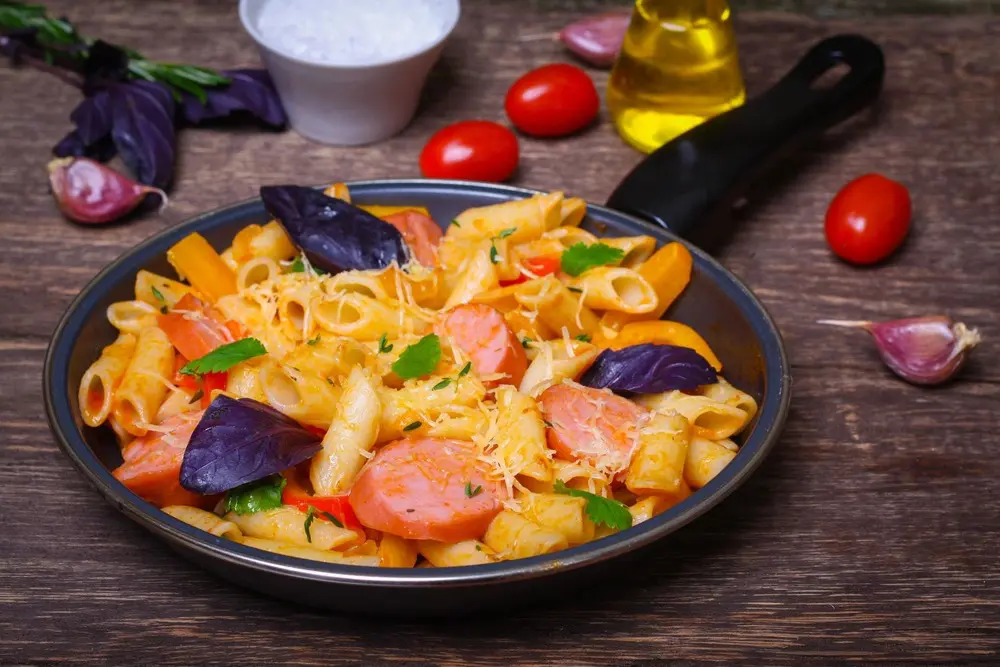 Pasta with sausage and basil in skillet.