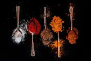 Spoons with colorful spices on dark background.