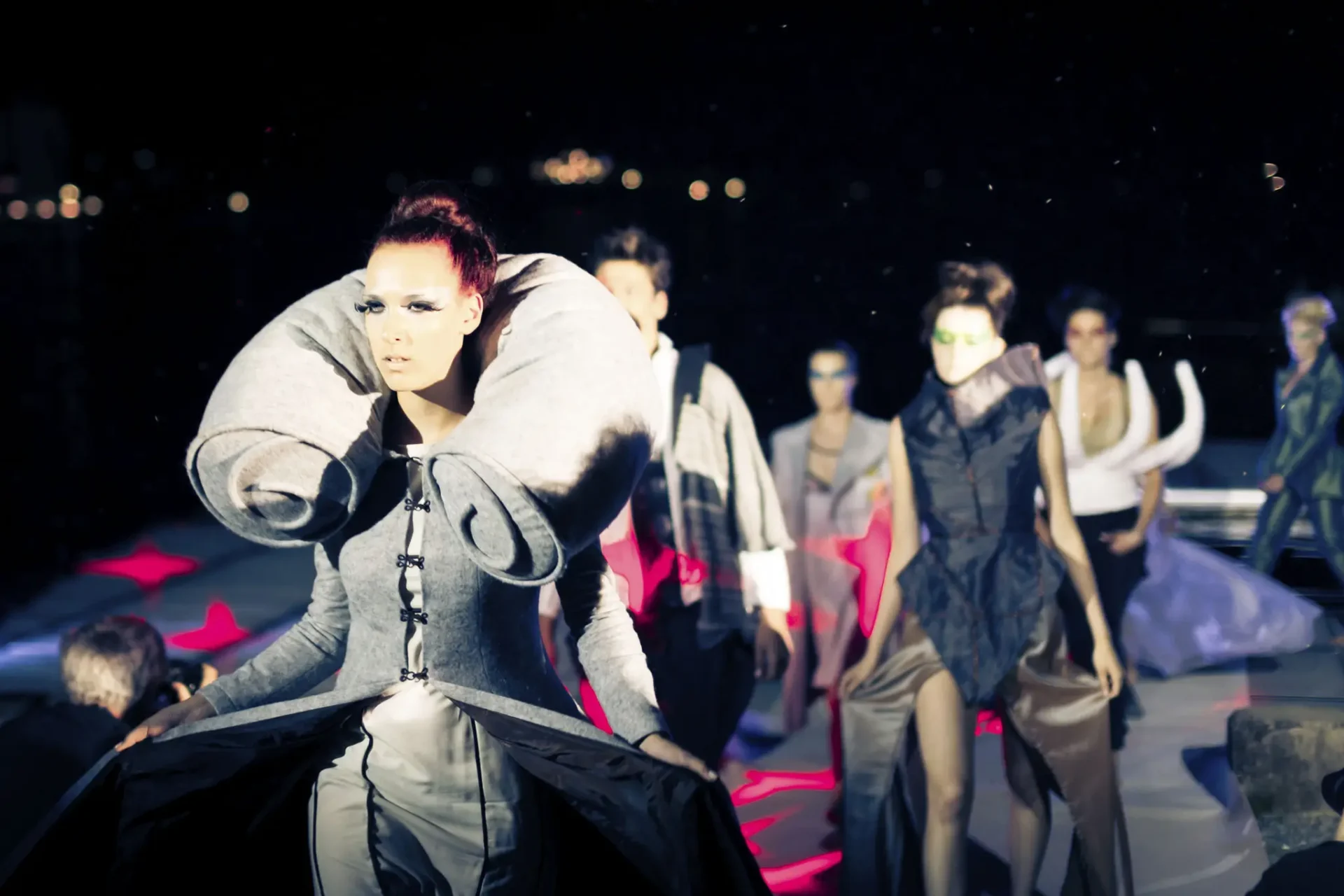 Avant-garde fashion models on a dimly lit runway.